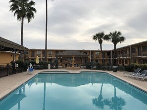 A swimming pool with lounge chairs, palm trees, and a building with balconies. - Americas Best Value Inn Laredo (Laredo)