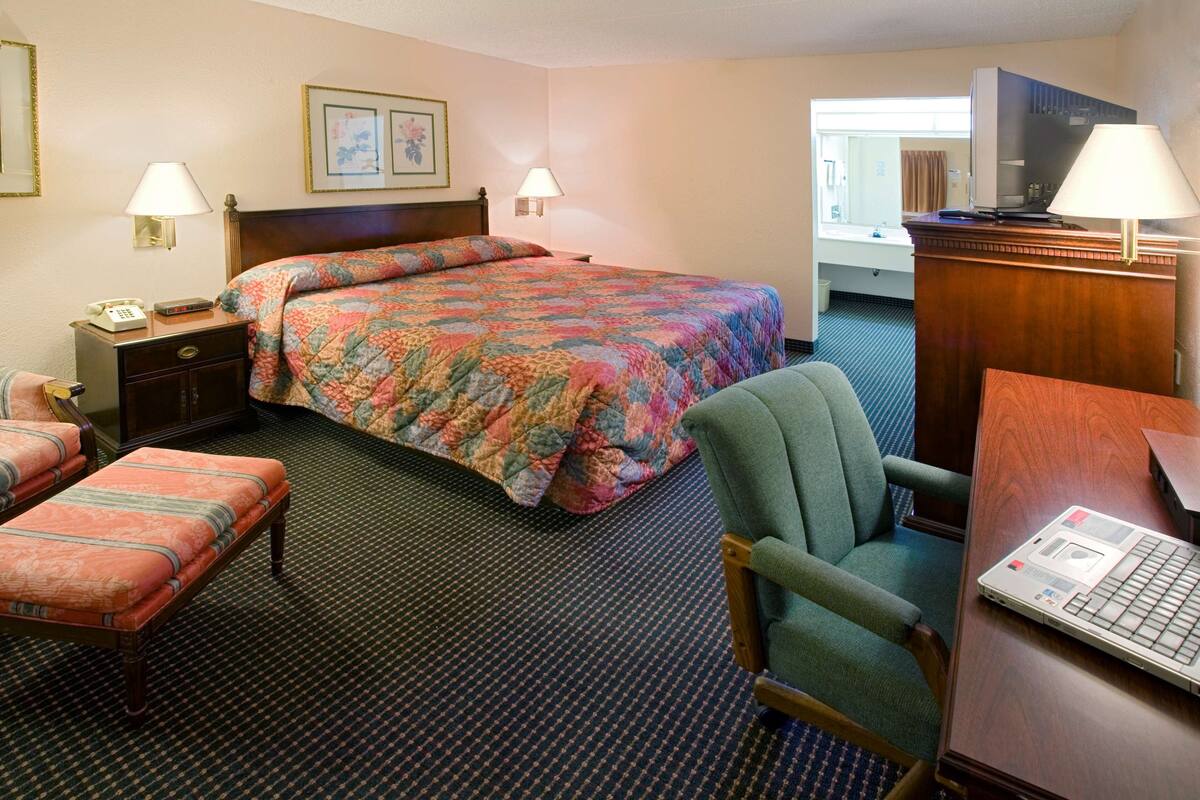Ein Hotelzimmer mit einem großen Bett, einem Schreibtisch mit einem Laptop, einem Sessel, einem Nachttisch mit einem Telefon und einem Spiegel.