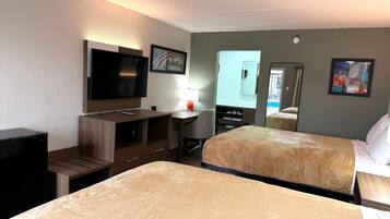 A hotel room with two beds, a TV, a desk with a chair, and a window with a view of a pool.