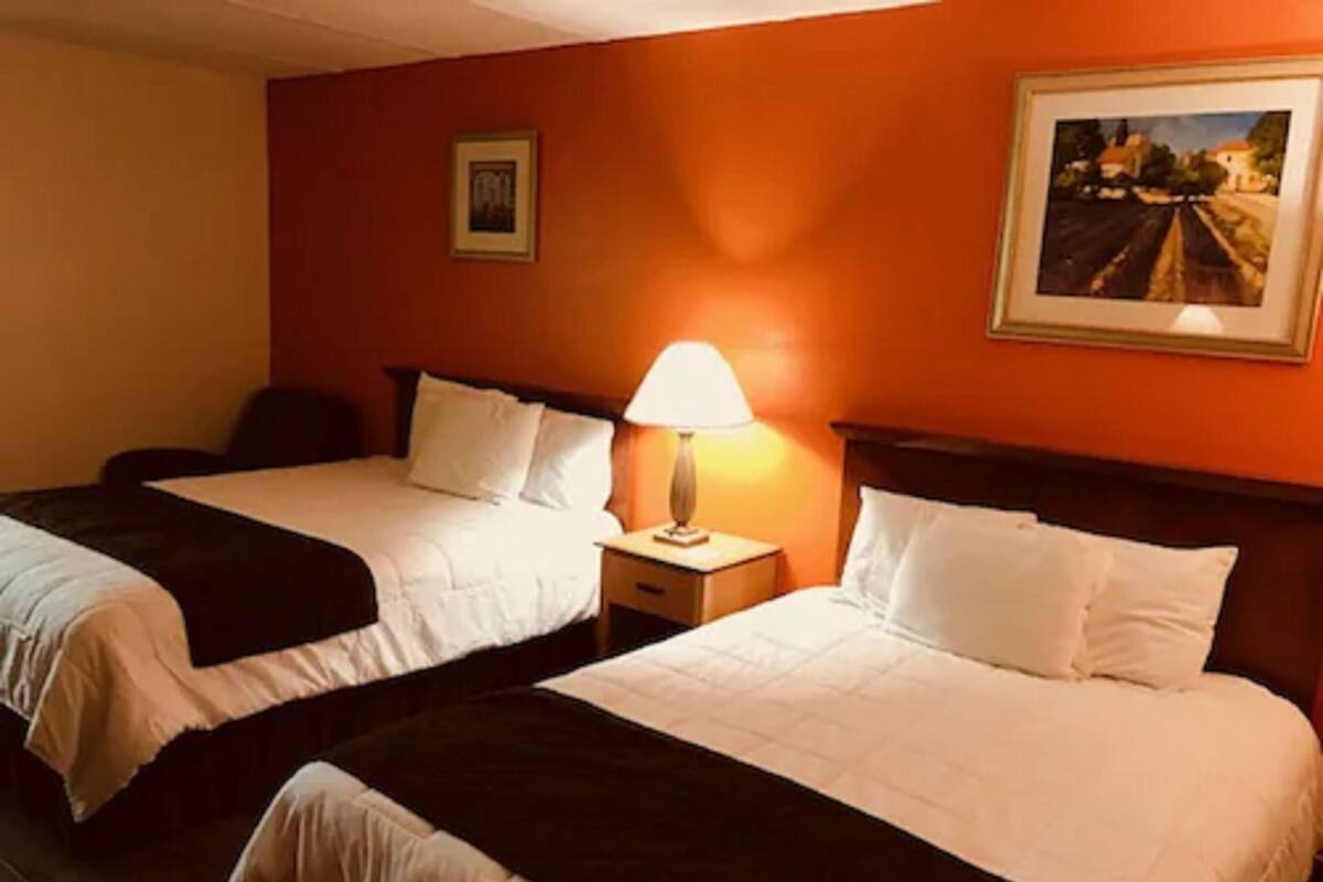 Ein Hotelzimmer mit zwei Betten, einem Nachttisch mit Lampe und einem gerahmten Bild an der Wand.