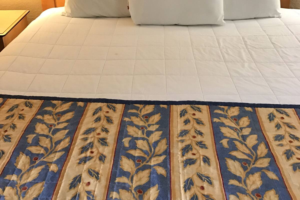 Ein ordentlich bezogenes Bett mit weißer Bettwäsche und einer zart gemusterten Tagesdecke.