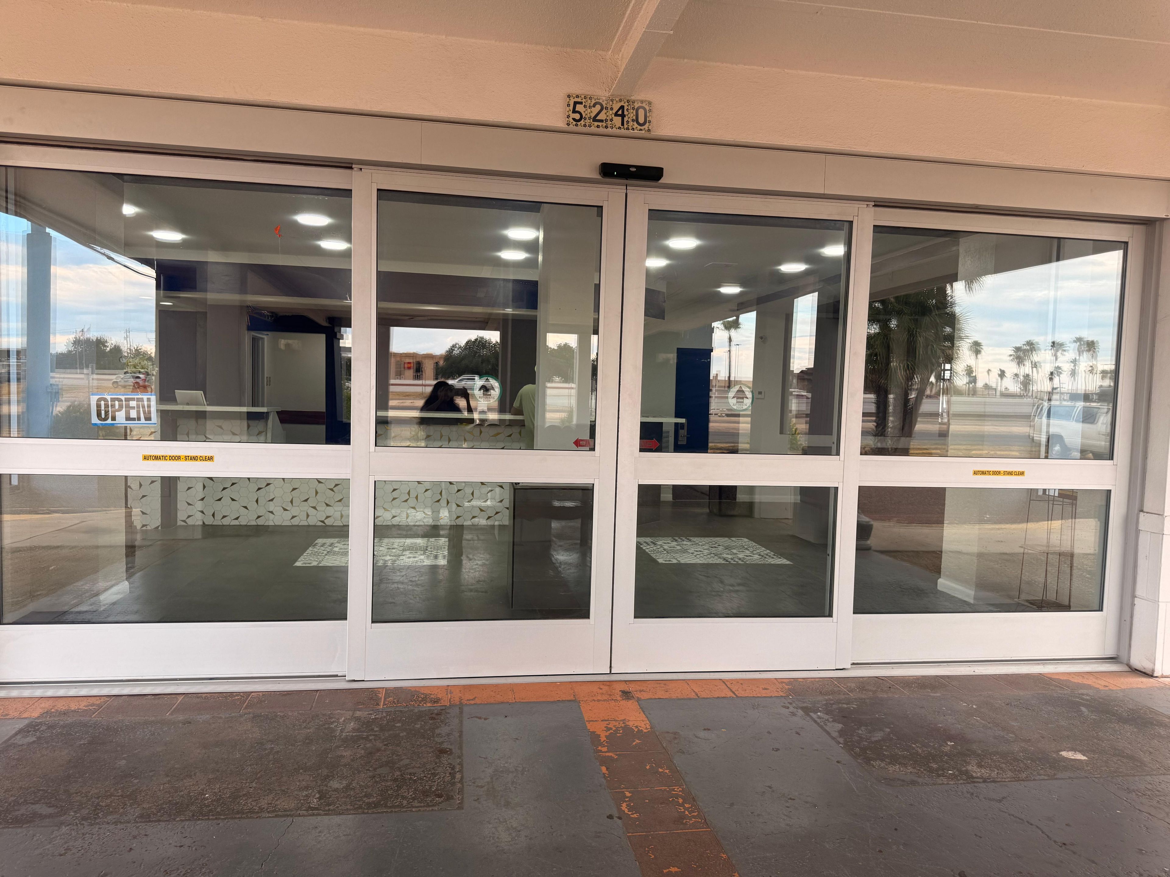 A building entrance with automatic doors, a clear sky, and a number sign above.