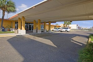 A gas station with a yellow building, a white car, and a palm tree. - Americas Best Value Inn Laredo (Laredo)