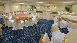 A conference room with round tables and chairs, carpeted floor, and wall-mounted lights. - Americas Best Value Inn Laredo (Laredo)