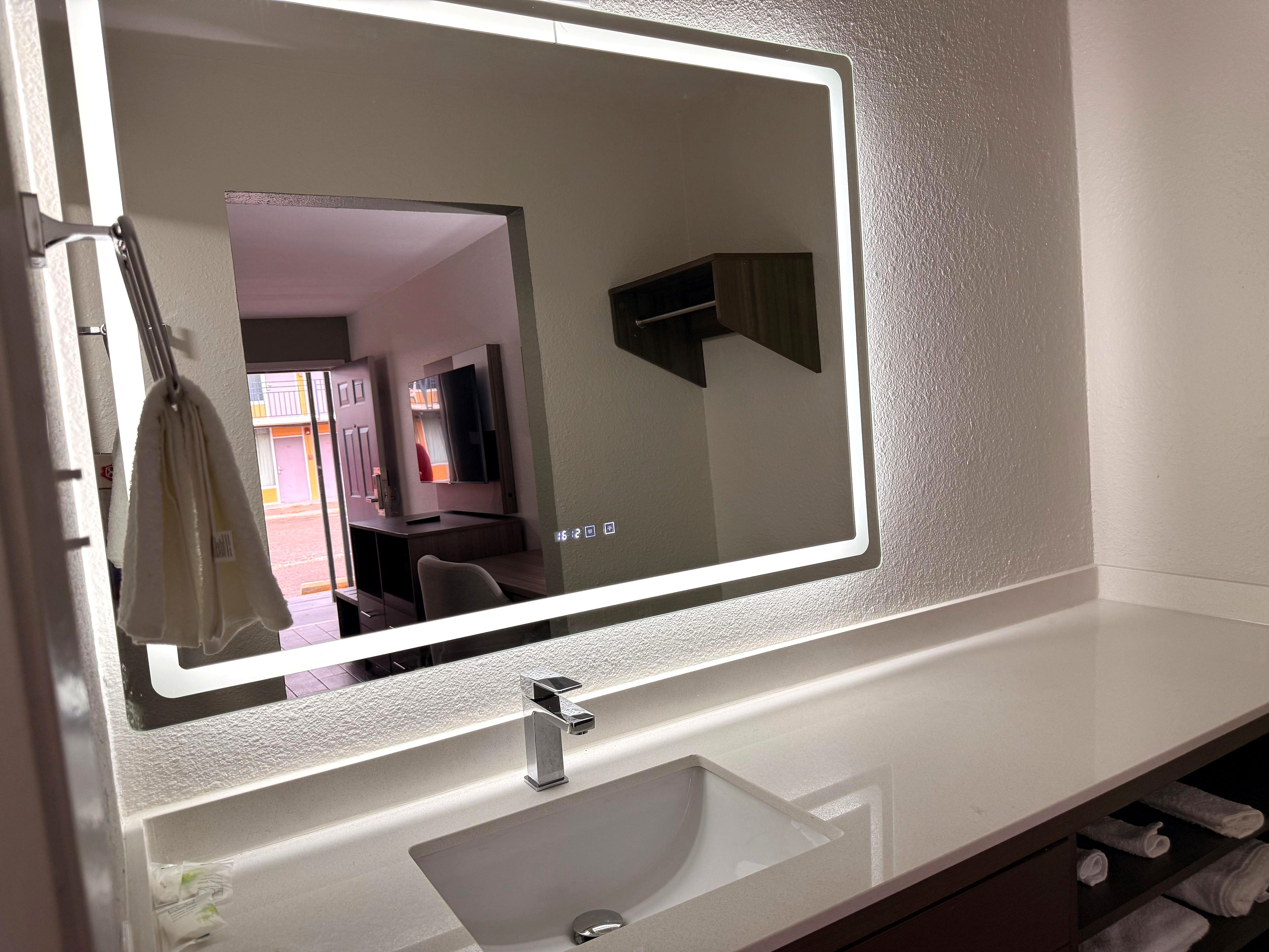 A bathroom with a large mirror, a sink, and a towel rack.