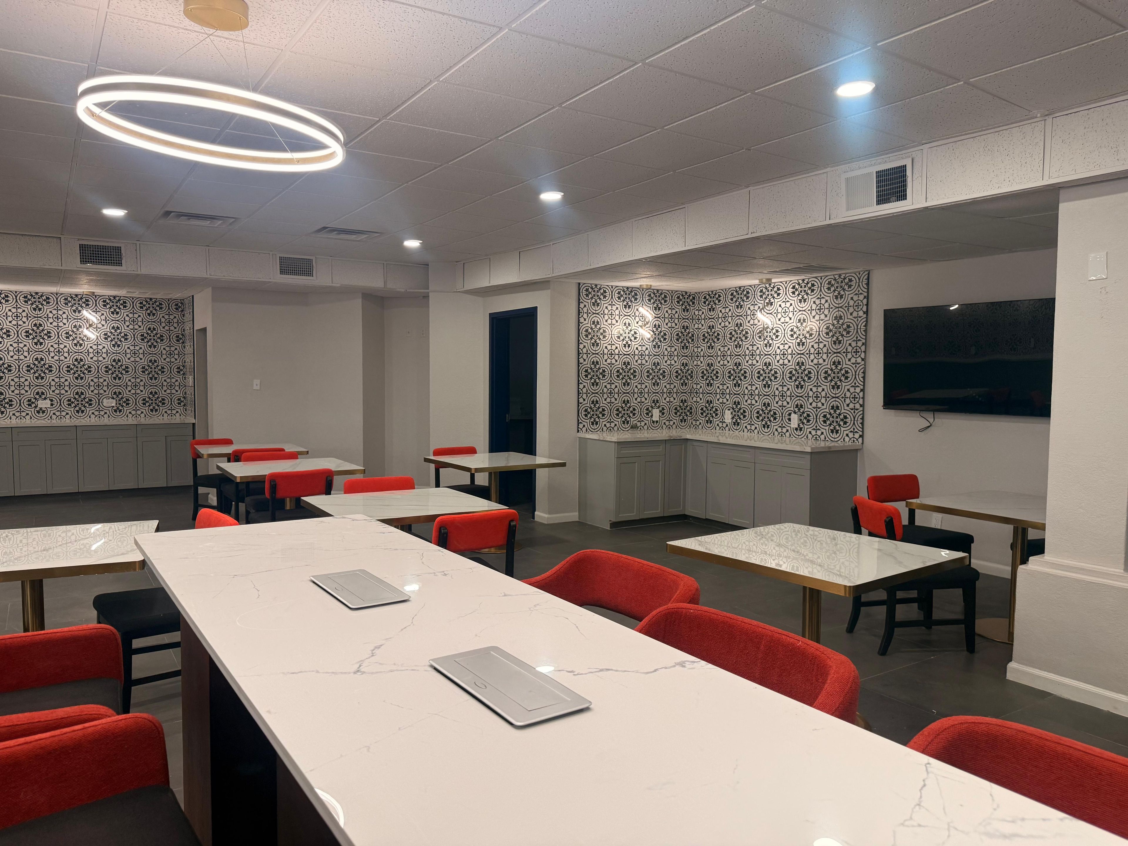 Una sala de conferencias moderna con mesas de mármol, sillas rojas y azulejos con diseños.