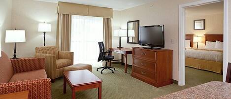 A hotel room with a sofa, armchair, desk, television, and a bed.