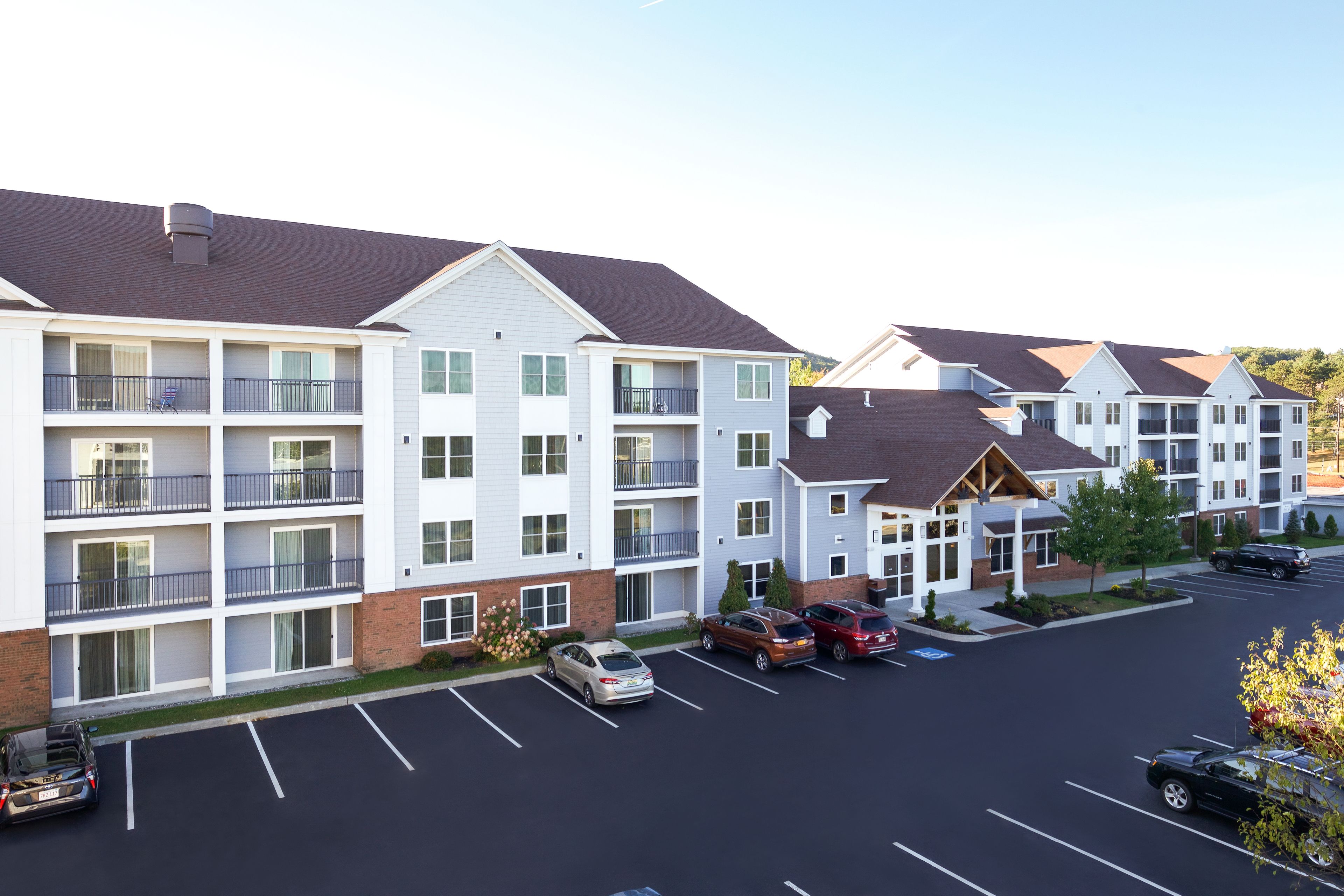 A multi-story hotel with a parking lot, featuring a mix of single and double rooms, a covered outdoor area, and a landscaped garden.