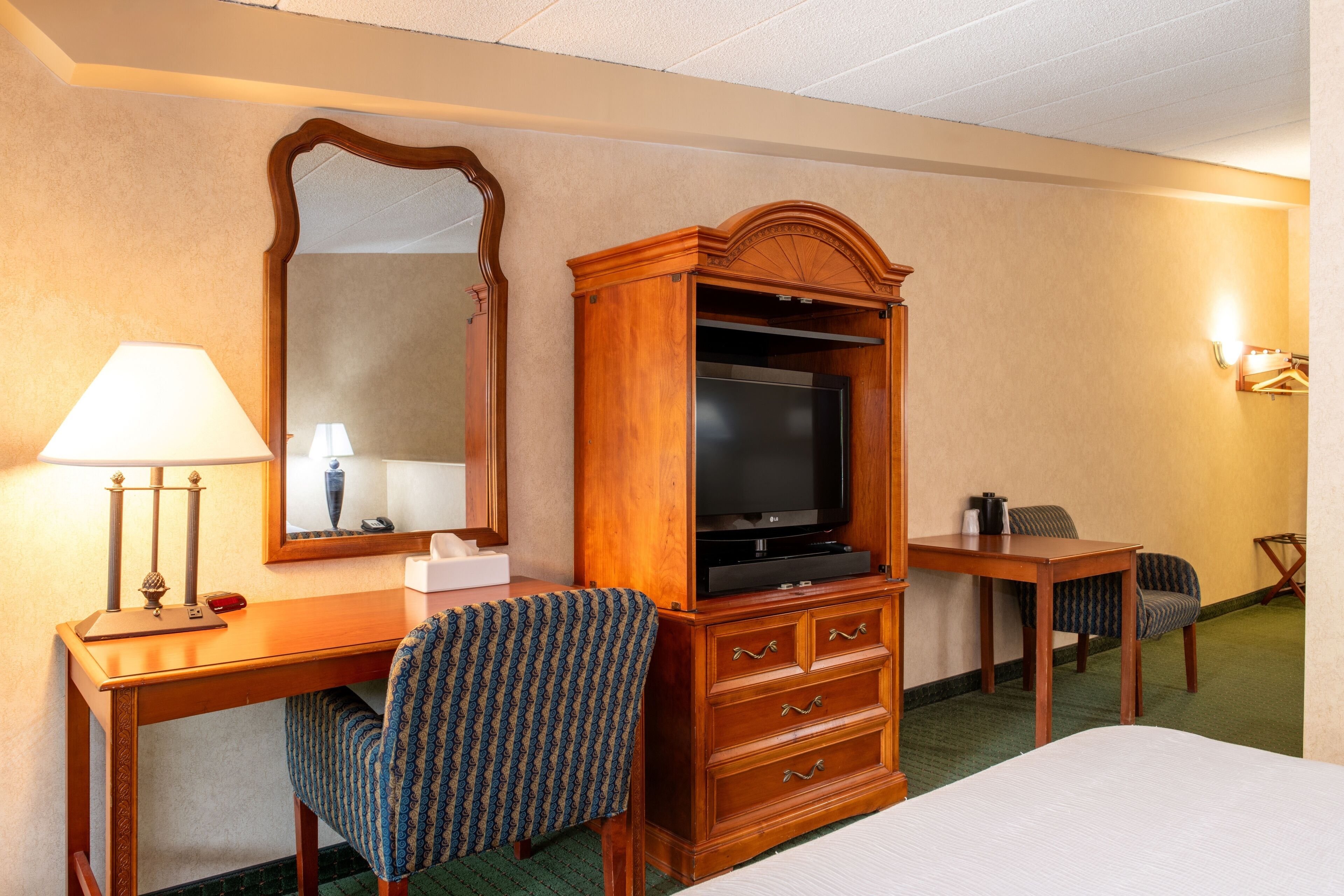 A hotel room with a wooden desk, a television, a chair, a bed, and a mirror.
