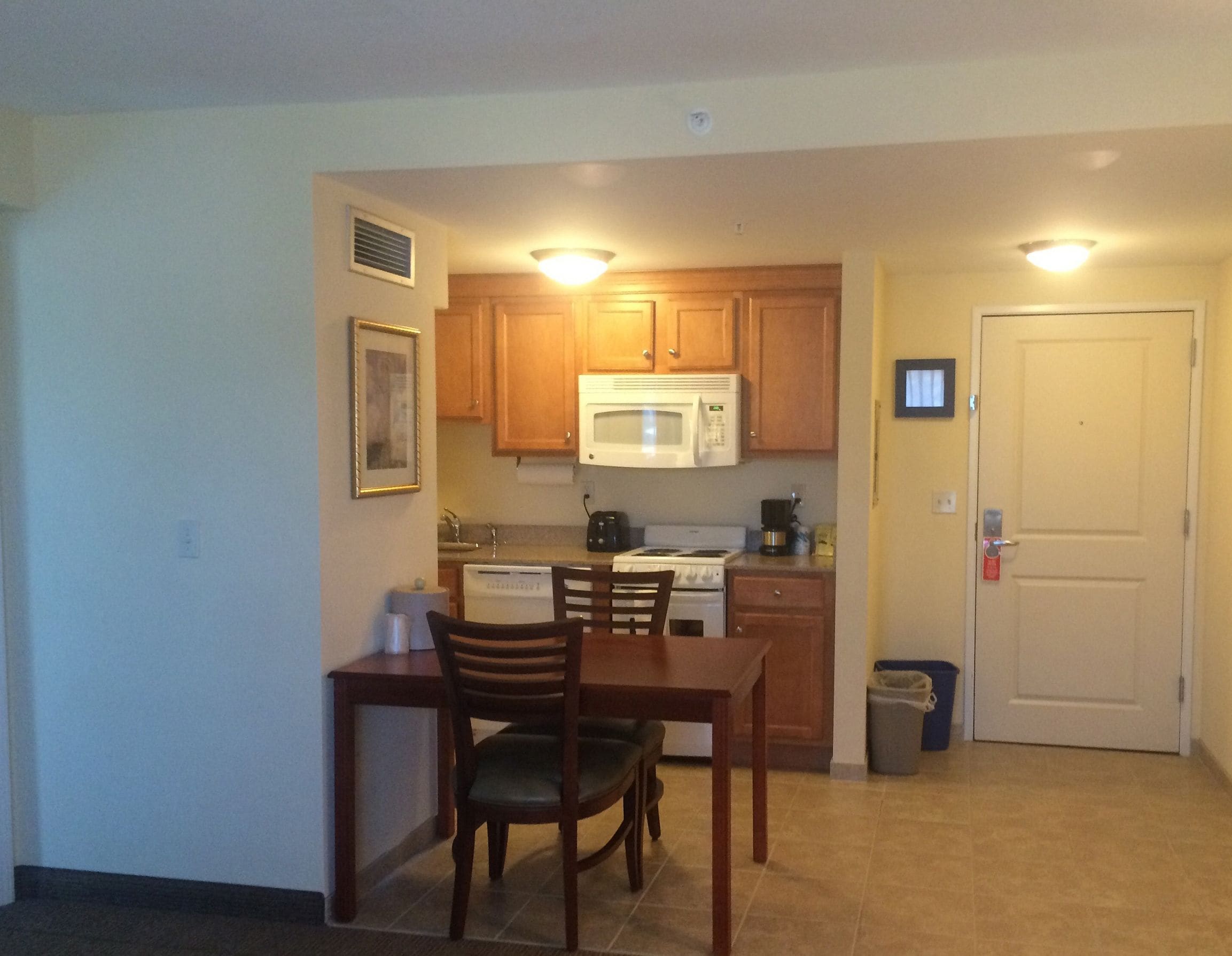 A compact kitchen with wooden cabinets, a microwave, a stove, and a dining area with two chairs.