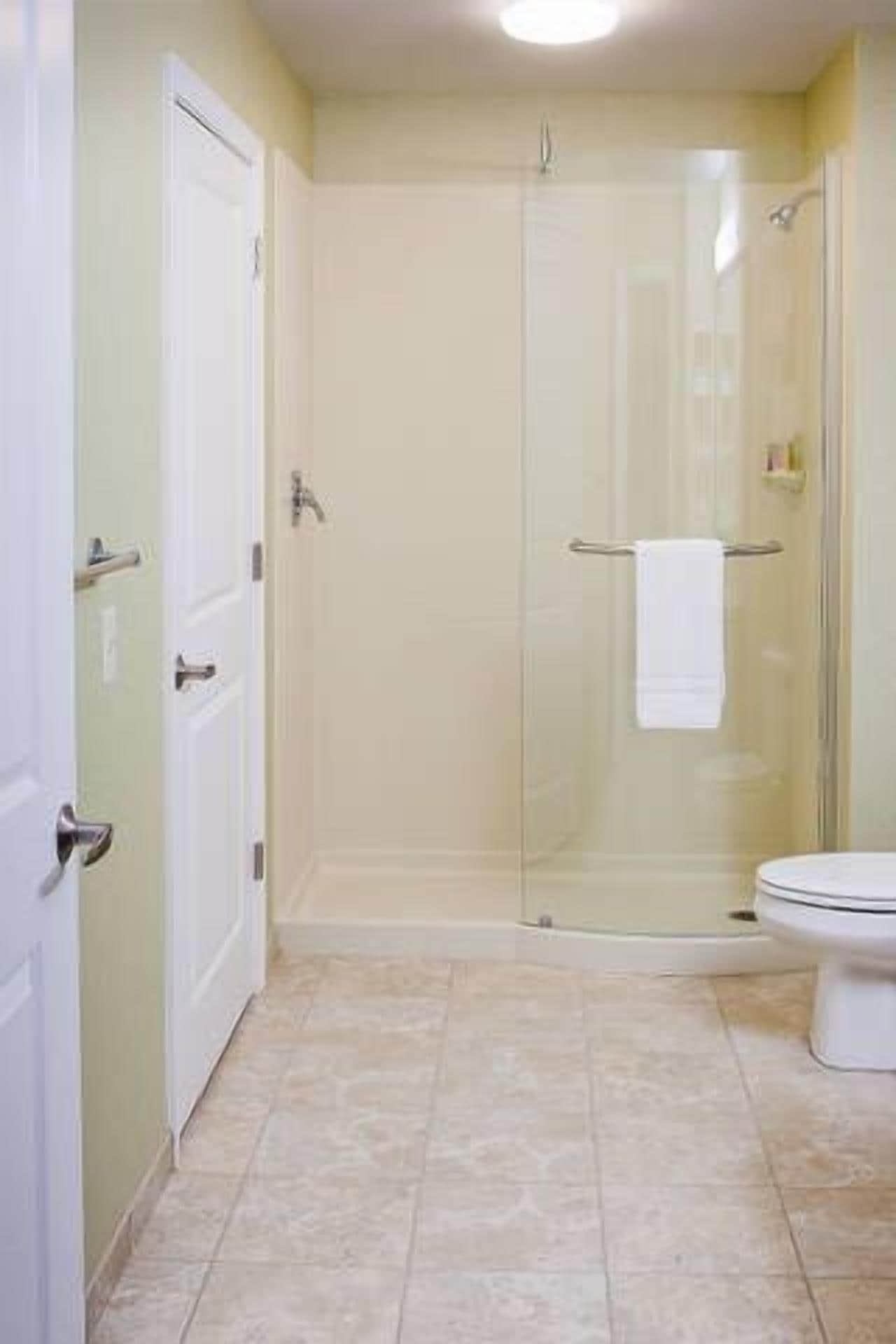 A bathroom with a glass-enclosed shower, a toilet, and a door.