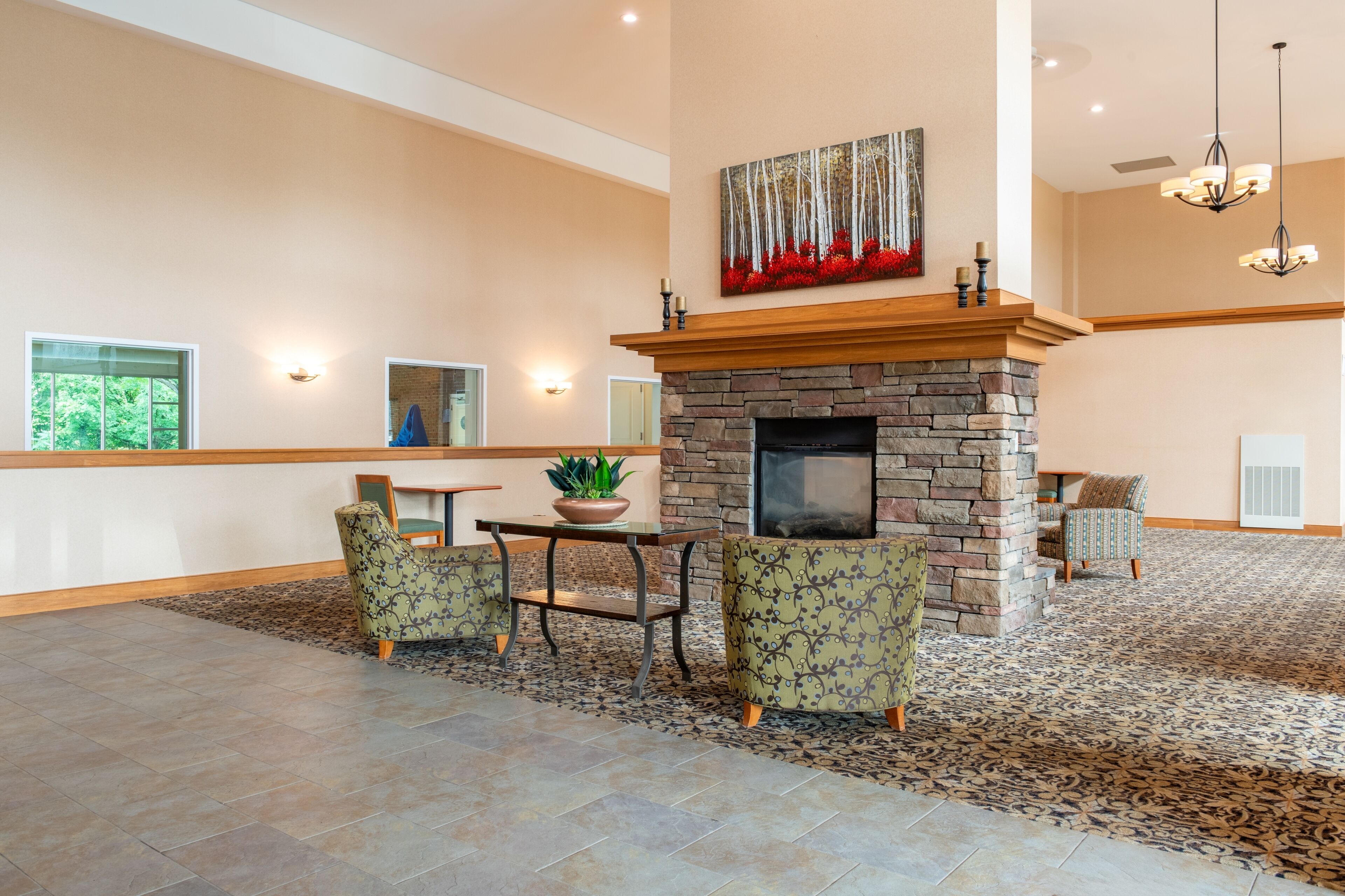 A spacious lobby with a stone fireplace, comfortable seating, and a large window offering a view of greenery.
