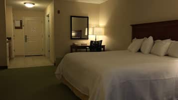 Une chambre d’hôtel avec un grand lit, un bureau avec une lampe, une chaise et un miroir au mur.