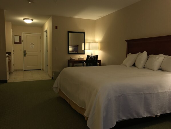 Una habitación de hotel con una cama grande, un escritorio con lámpara, una silla y un espejo en la pared.