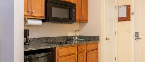 A kitchen with wooden cabinets, a stainless steel dishwasher, a black microwave, and a granite countertop.