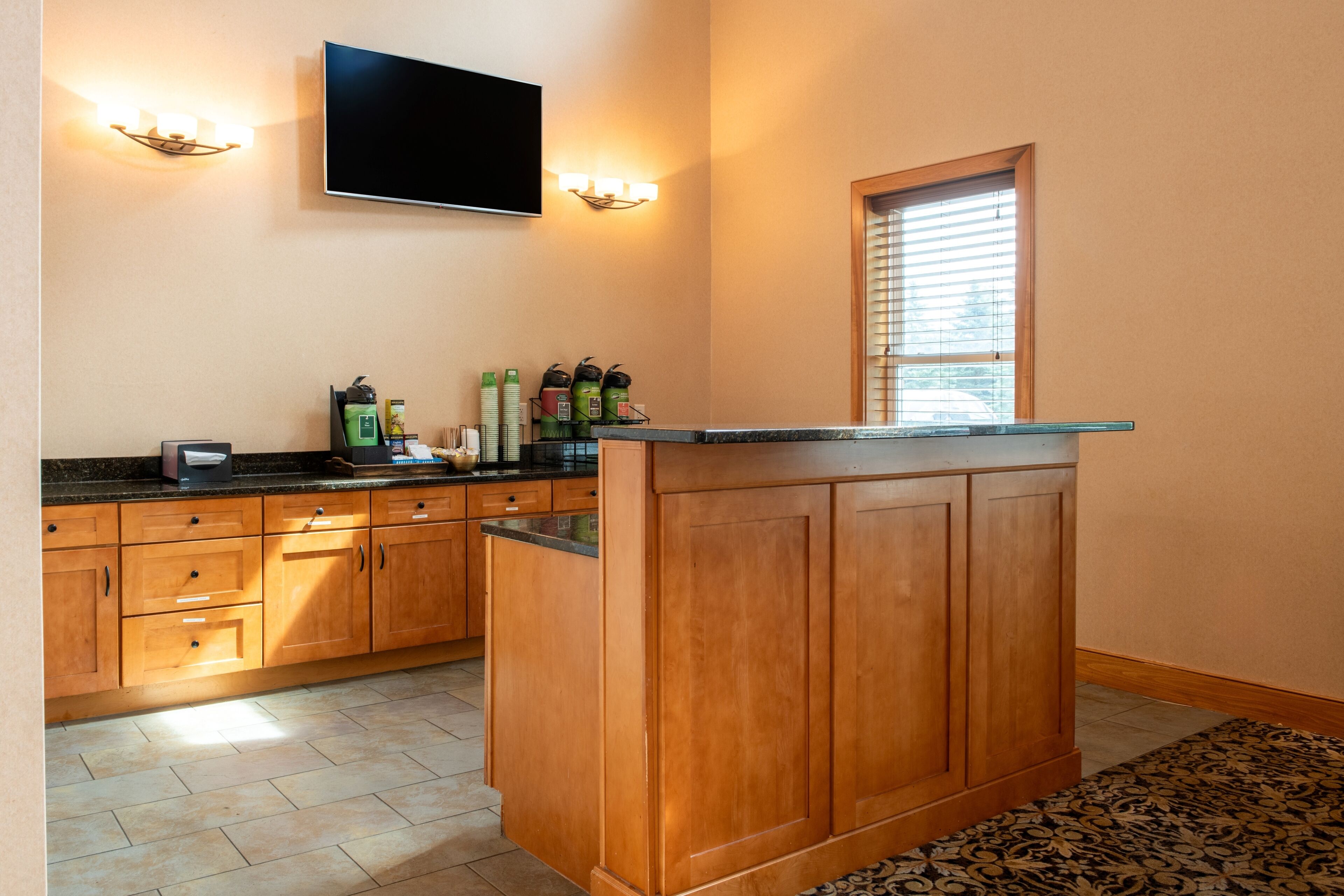 A kitchen with wooden cabinets, a granite countertop, a built-in island, a flat-screen TV, and wall-mounted sconces.