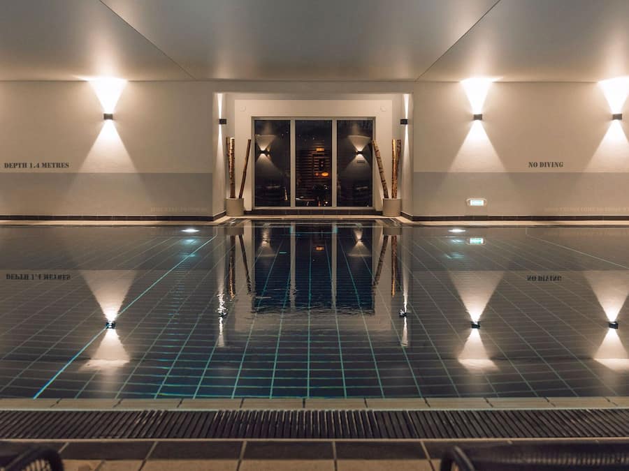 Ein Innenpool mit klarem Wasser, umgeben von Wänden mit Text und Beleuchtung.