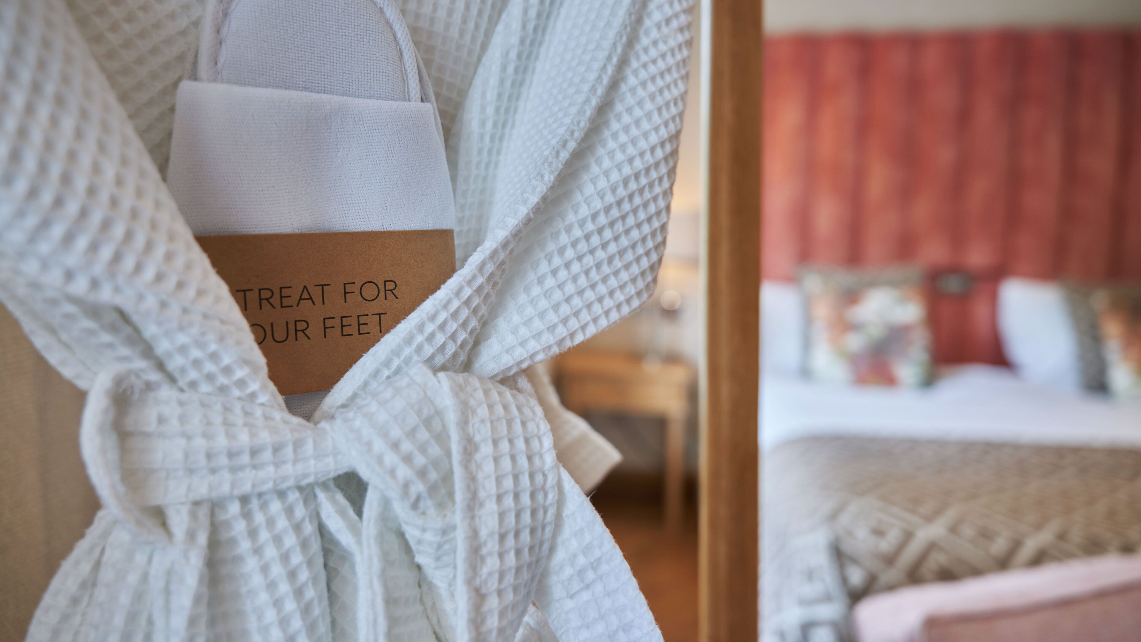 A white bathrobe with a label reading "TREAT FOR OUR FEET" hanging on a door.