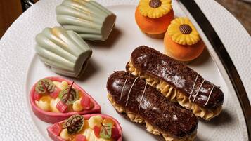 A plate with various pastries, including a chocolate-covered pastry with cream filling and a pink pastry with fruit and leaves.
