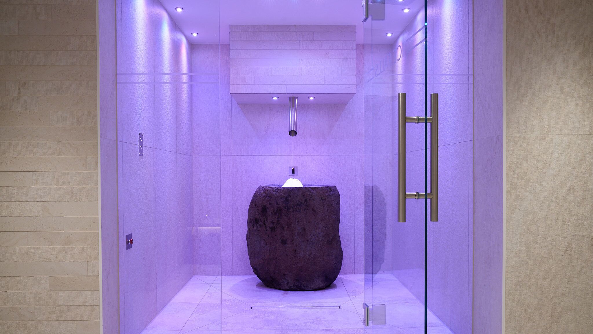 A modern, glass-walled shower stall with a central stone pedestal, recessed lighting, and a minimalist design.