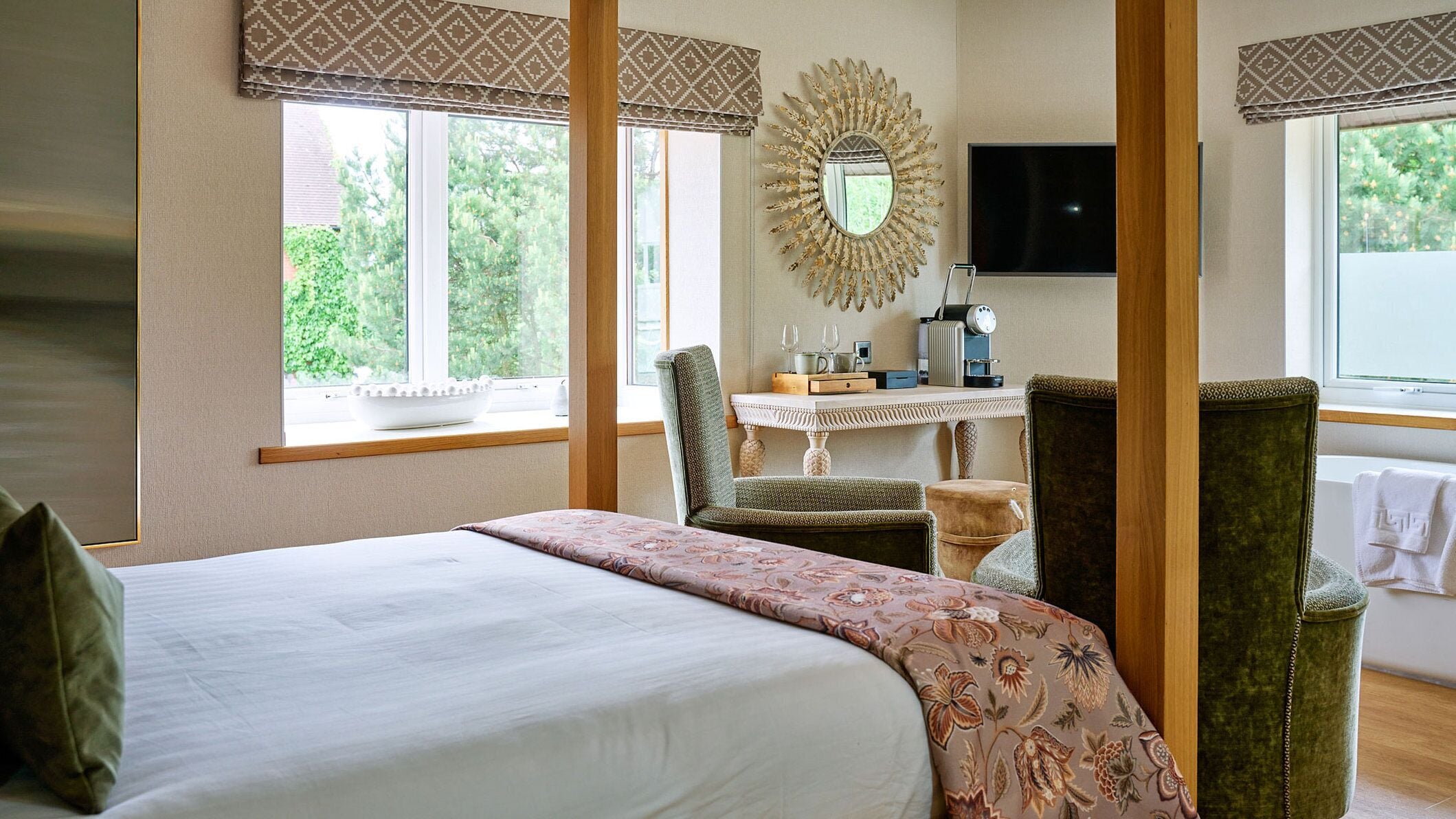A bedroom with a large bed, a chair, a small table with a mirror, and a television on the wall.