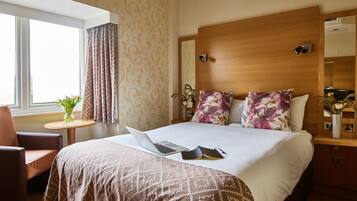 A hotel room with a large bed, a laptop, a book, and a vase with flowers on the nightstand.