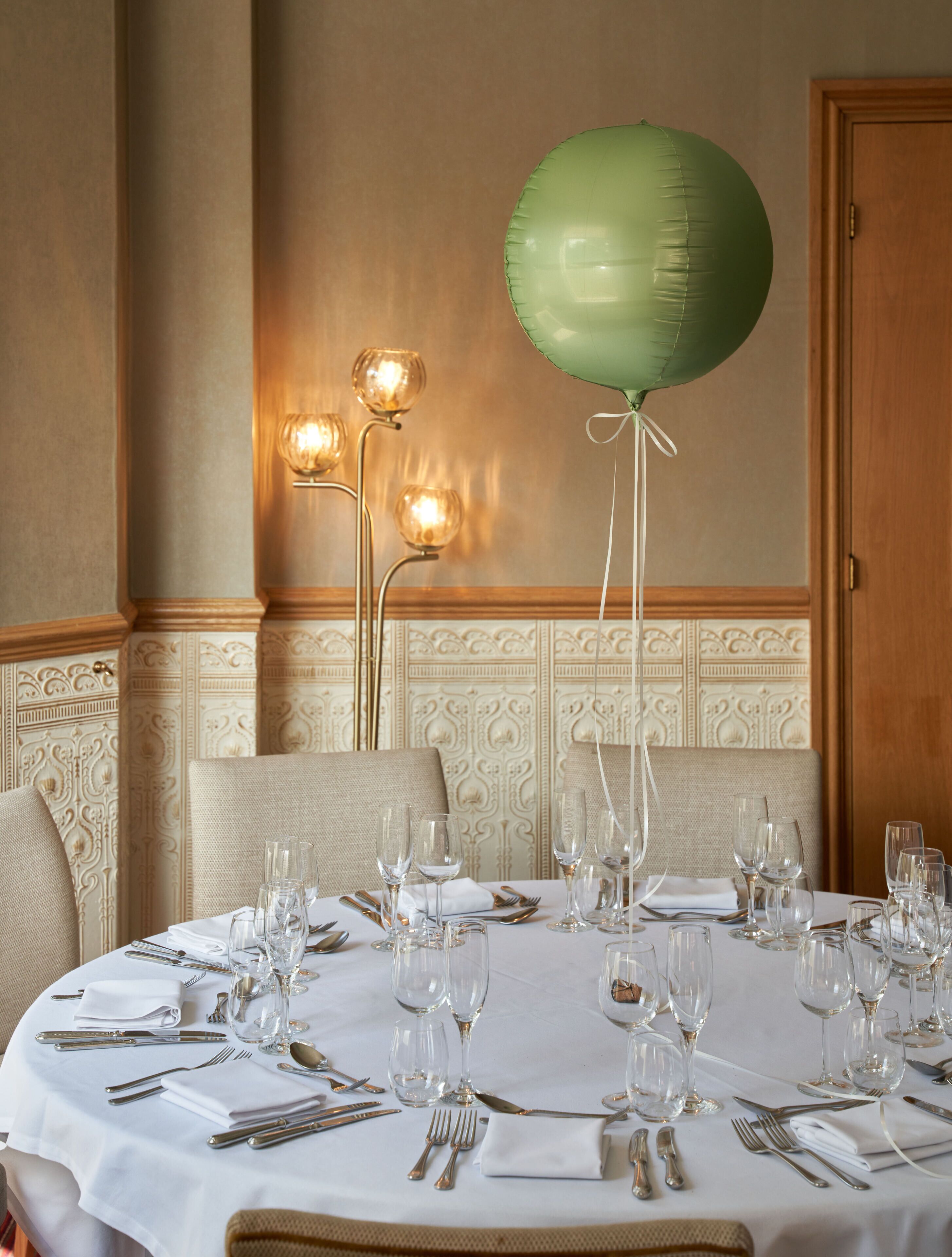 A dining table set for a meal with a green balloon, elegant table settings, and decorative wall sconces.