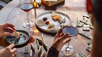 Un grupo de personas jugando dominó alrededor de una mesa, con copas de vino y platos de queso.