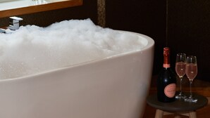 A large bathtub filled with bubbles, a vase with flowers, and two glasses of wine on a small table. - Fairlawns Hotel and Spa (Walsall)