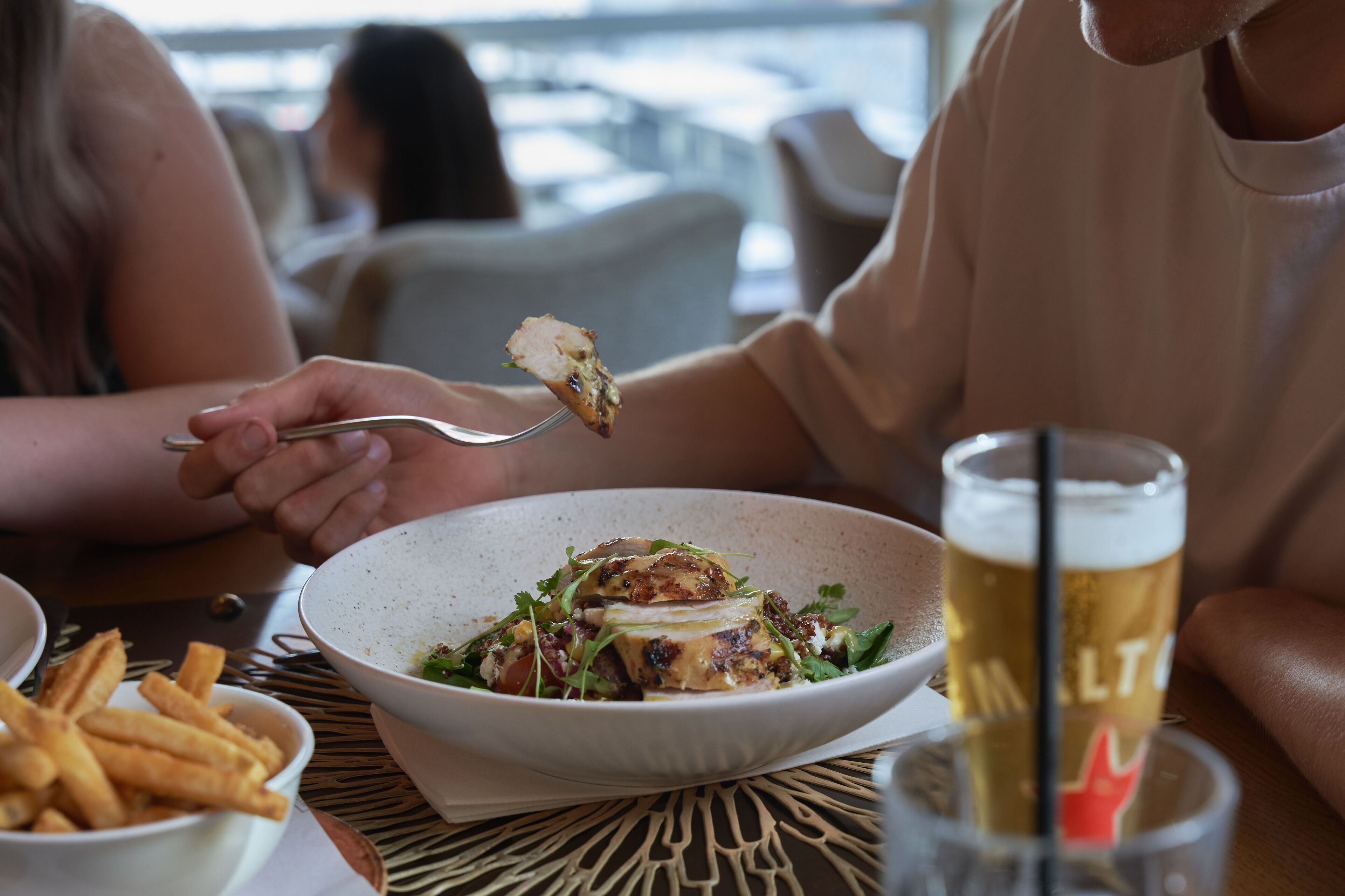 Uma mesa de jantar com uma salada numa tigela, um copo de cerveja e batatas fritas num prato.