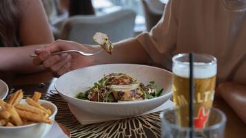 Uma mesa de jantar com uma salada numa tigela, um copo de cerveja e batatas fritas num prato.
