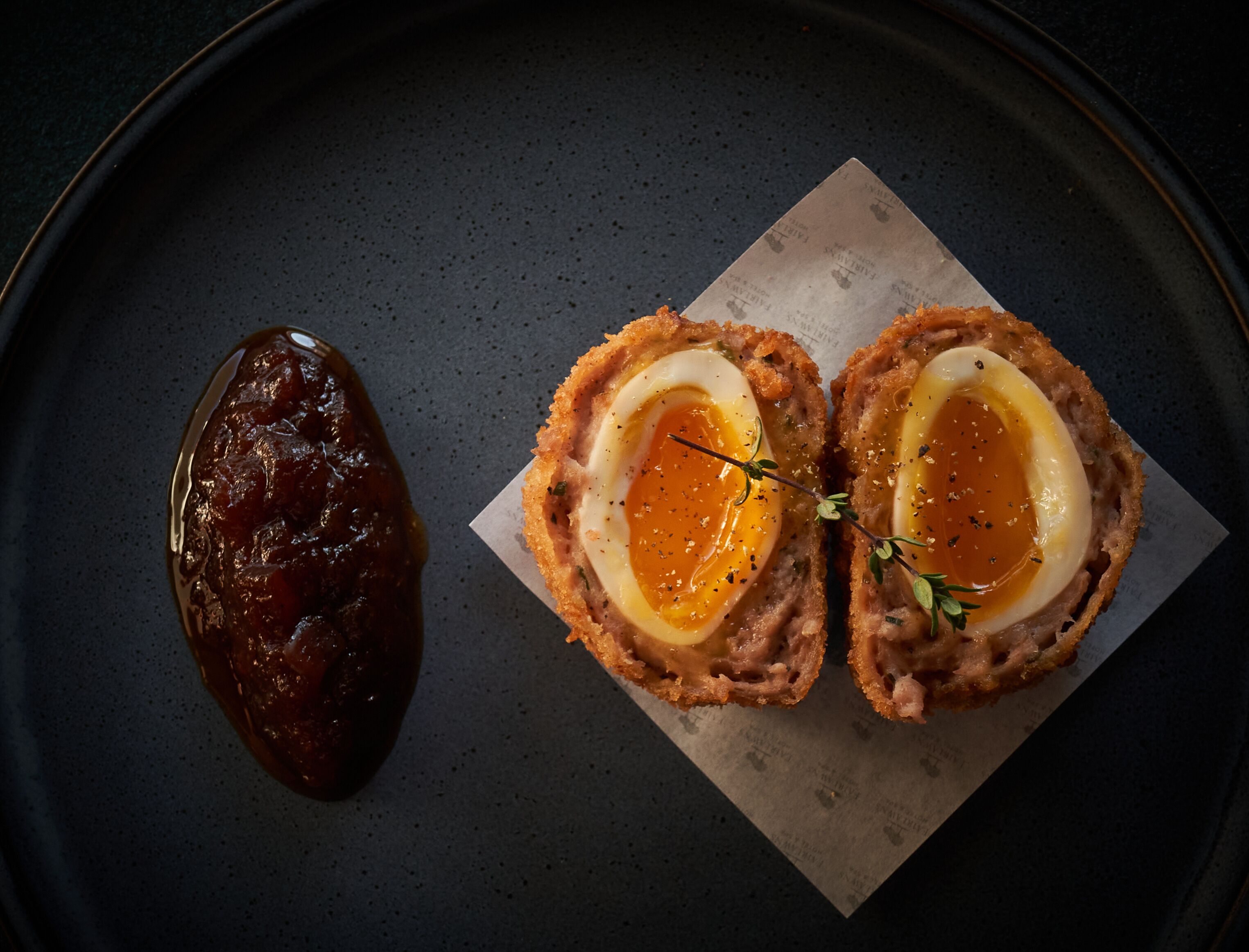 Plato con exterior crujiente e interior tierno, servido sobre un plato oscuro con un trozo de carne oscura al lado.