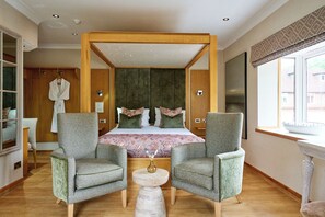 A bedroom with a large bed, two armchairs, a small table, and a window with a view. - Fairlawns Hotel and Spa (Walsall)