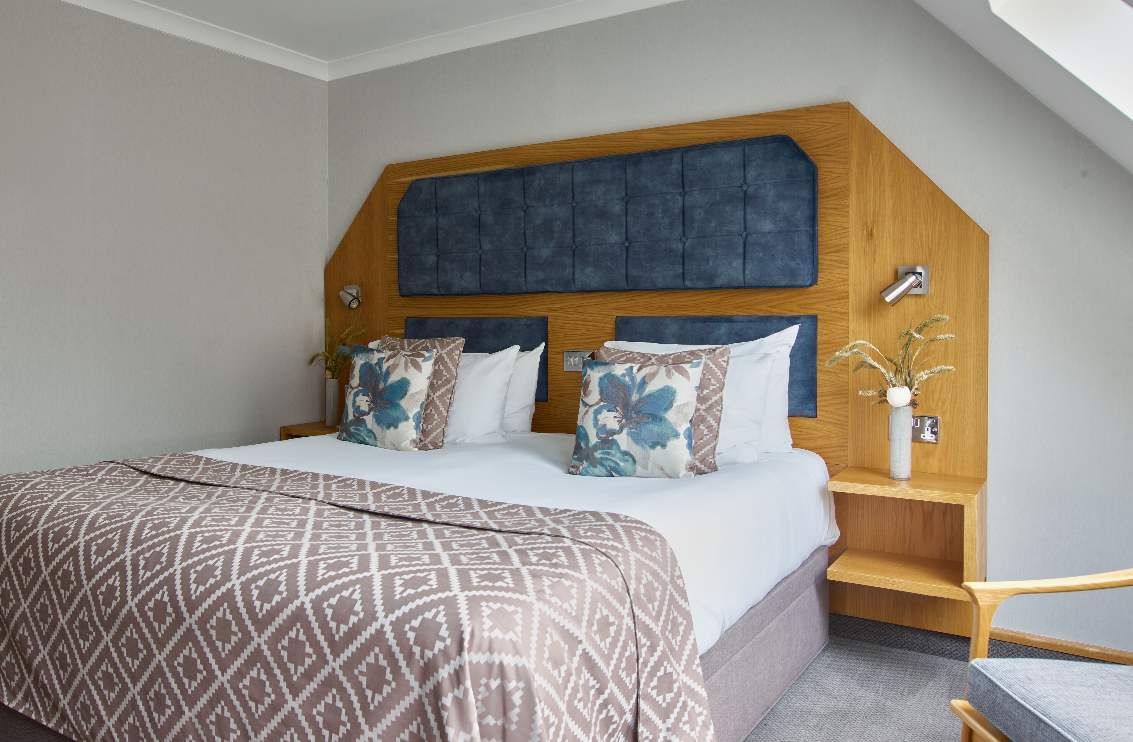 A bedroom with a large bed, a wooden headboard, and a bedside table with a vase.