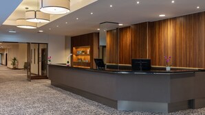 Un área de recepción con diseño moderno, que incluye un mostrador de recepción, zona de estar y plantas decorativas.