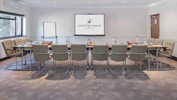 A conference room with a long table, six chairs, and a projector screen displaying 'Stratford Manor The Ghotels Collection'.