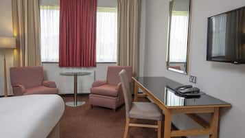 Habitación de hotel con cama, dos sillones, una mesita, un escritorio con teléfono y televisor en la pared.
