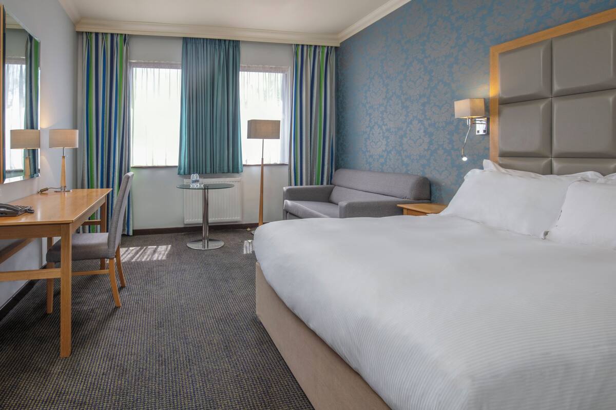 Ein Hotelzimmer mit einem großen Bett, einem Schreibtisch mit Stuhl, einem kleinen Tisch und einem Sofa.