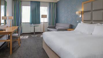 Una habitación de hotel con una cama grande, un escritorio con una silla, una mesita pequeña y un sofá.