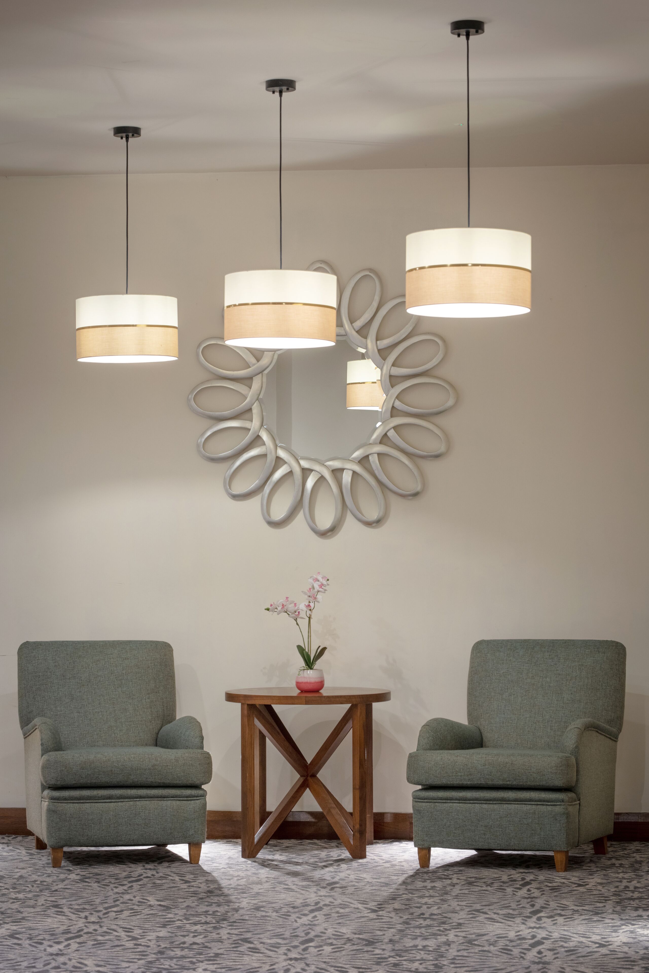 Ein Zimmer mit zwei grünen Sesseln, einem Holztisch mit einem Blumentopf und einer modernen Wandleuchte.