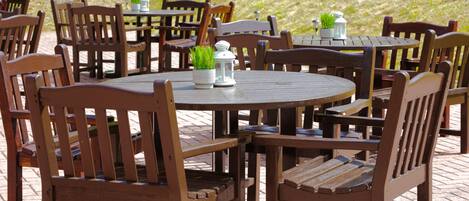 A round wooden table with chairs around it, some with potted plants on them.