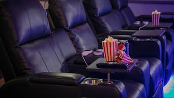 Filas de asientos de cuero negro en un cine, con reposabrazos individuales, cada uno con una mesita que sostiene un balde de palomitas y un control remoto.
