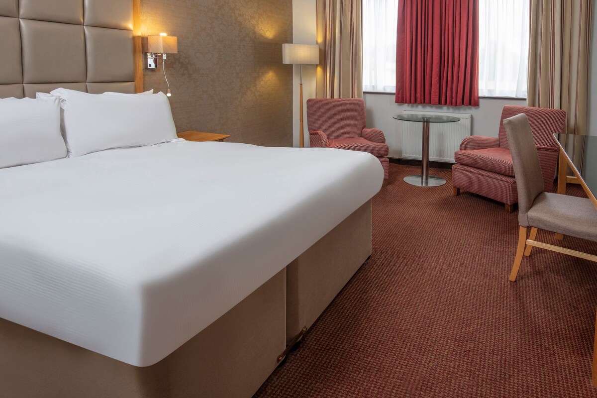 A hotel room with a large bed, two armchairs, a small round table, and a lamp.