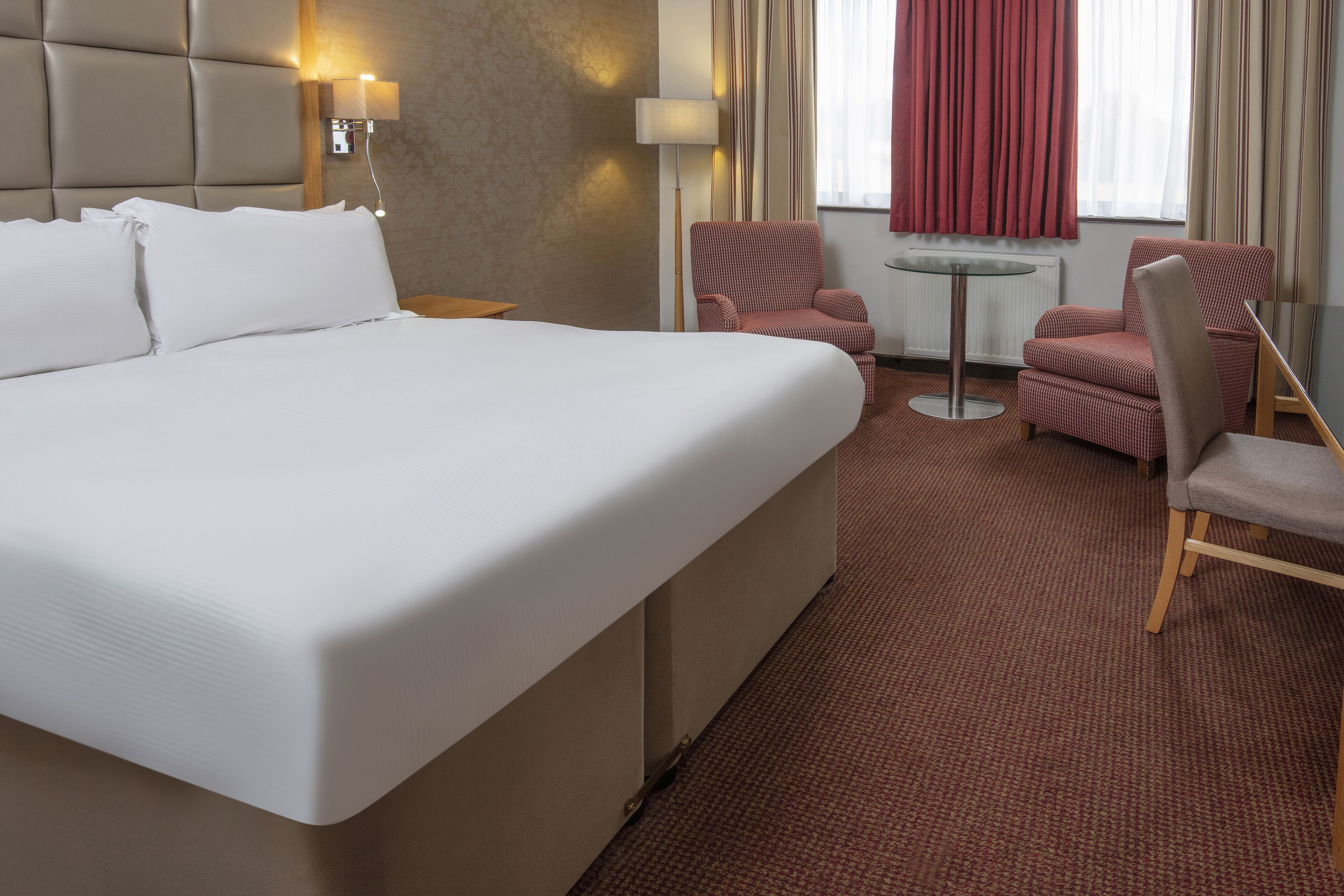 A hotel room with a large bed, two armchairs, a small table, and a lamp.