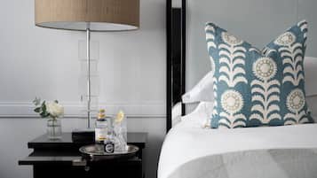 A neatly arranged hotel room with a bed, a bedside table with a lamp, a vase with a flower, and a tray with bottles.