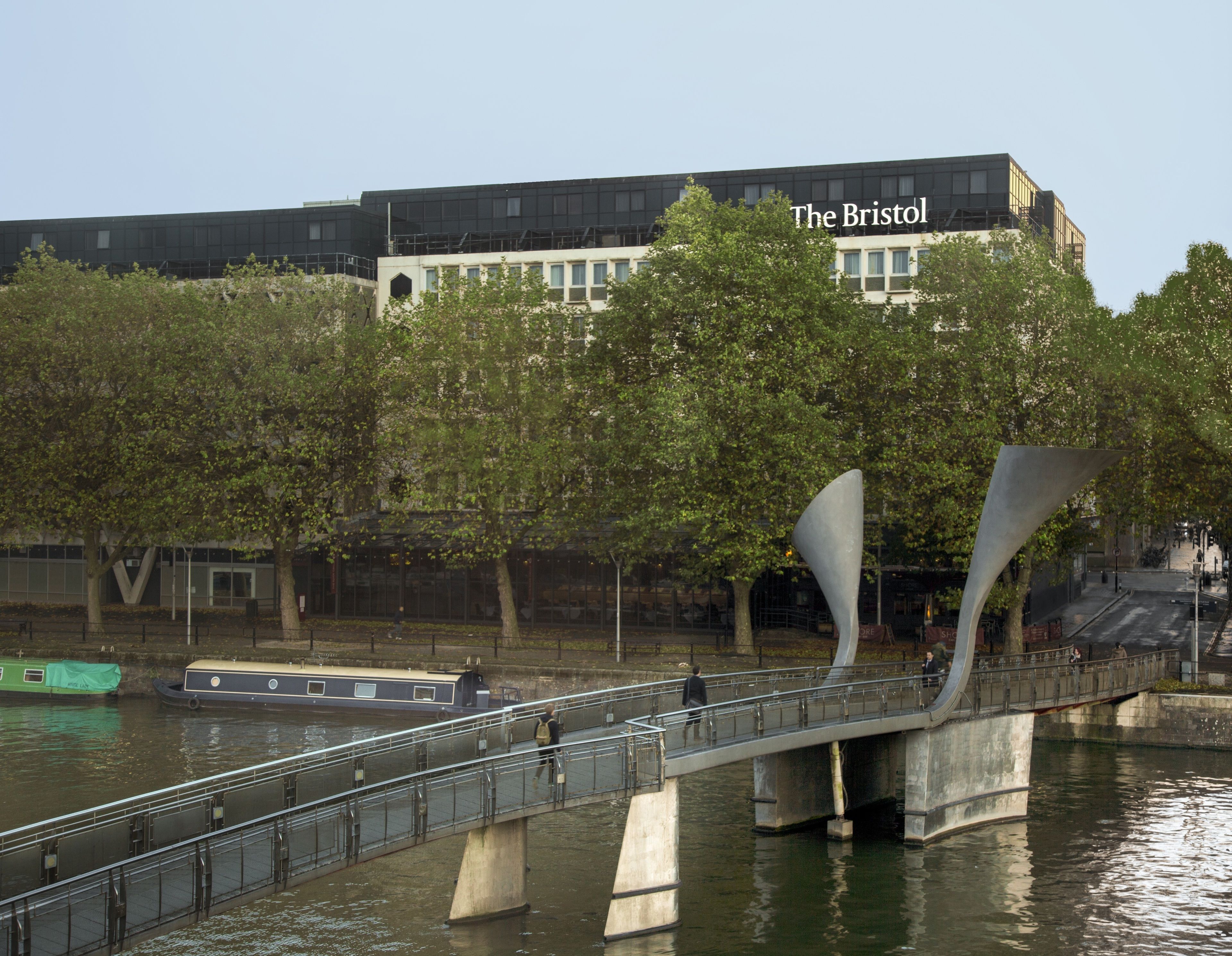 A modern bridge with a unique design, a river, and a building labeled "The Bristol" in the background.