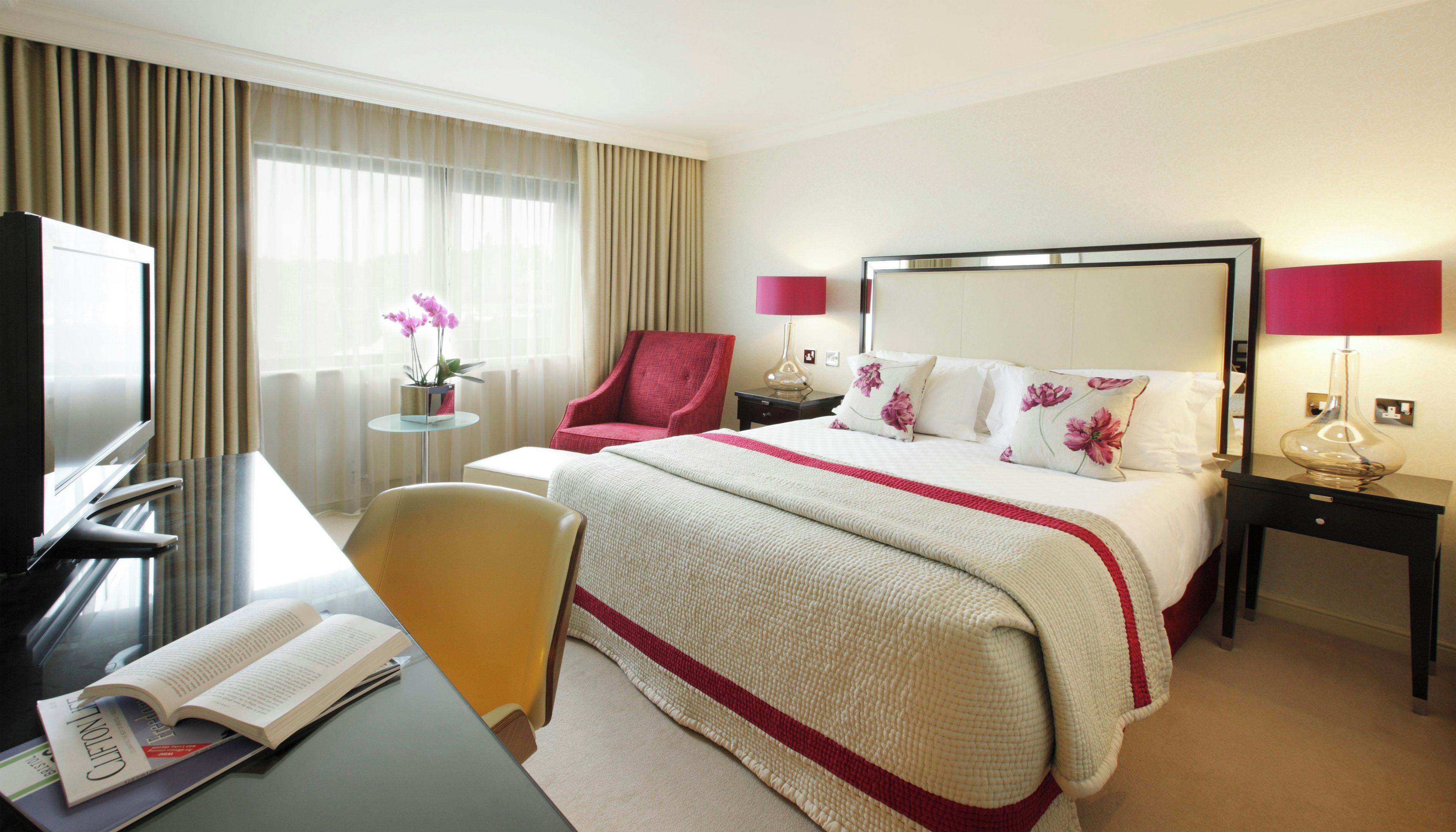 Una habitación de hotel con una cama, un escritorio con una silla, un televisor y una ventana con cortinas.