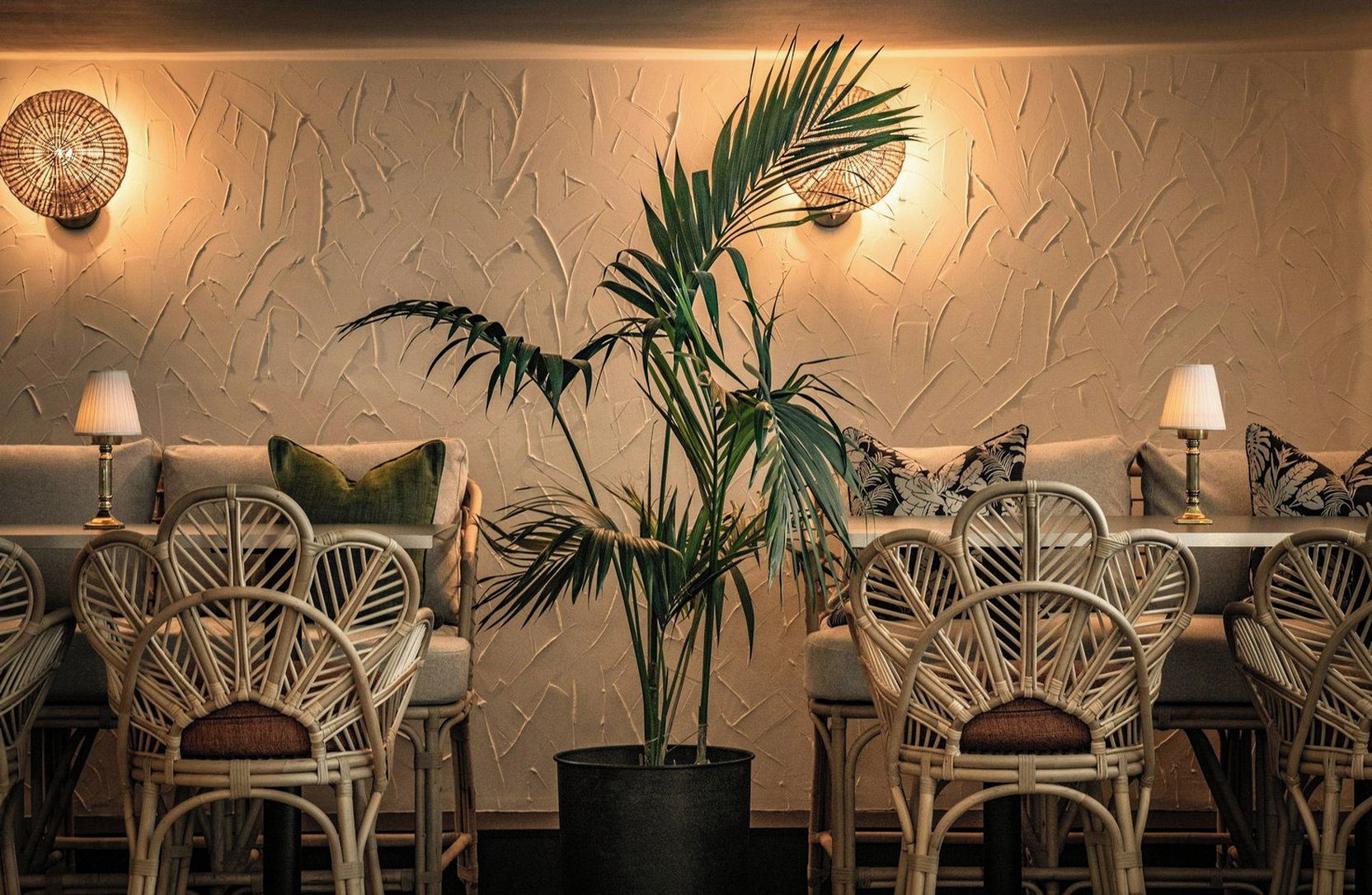 A room with a sofa, chairs, a potted plant, and wall sconces.
