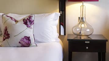 A neatly made bed with a red blanket, a white pillow with a floral design, and a bedside table with a red lampshade.