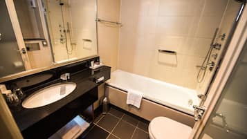 A modern bathroom with a large mirror, a sink, a bathtub, and a toilet.